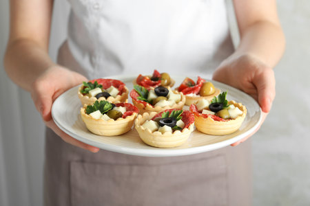 Woman holding plate with tasty canapes on light gray background, closeupの写真素材