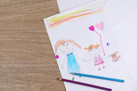 Child's drawing of happy family and pencils on wooden table, top viewの写真素材