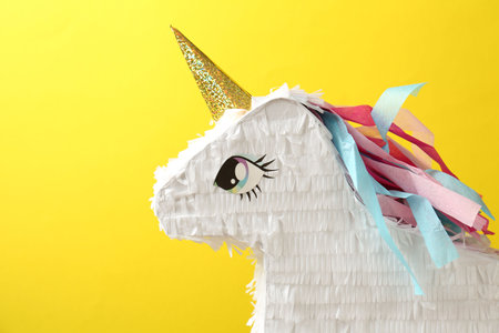 Beautiful pinata in shape of unicorn on yellow background, closeup. Space for textの写真素材