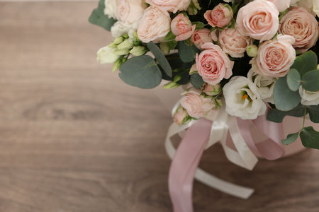Gift box with bouquet of beautiful flowers and eucalyptus branches on wooden table, closeup. Space for textの写真素材