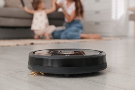 Mother spending time with her daughter in room, focus on robotic vacuum cleanerの写真素材