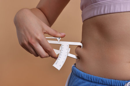Woman measuring body fat with caliper on beige background, closeupの写真素材