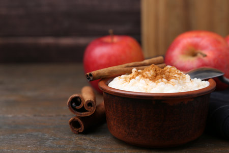 Delicious rice pudding with cinnamon sticks and apples on wooden table, closeup. Space for textの写真素材