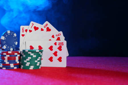 Poker chips and playing cards on pink table in neon lights, space for textの写真素材