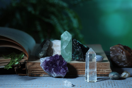 Beautiful natural gemstones and book on grey table against green background