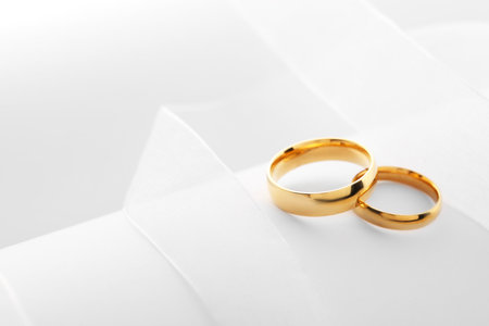 Beautiful golden wedding rings and white ribbon on light backgroundの写真素材