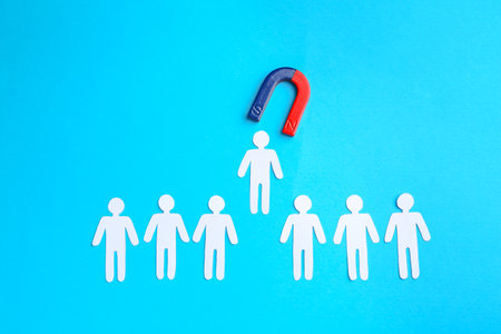 Magnet attracting paper cutouts of humans on light blue background, flat layの写真素材