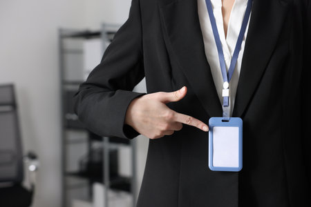 Woman pointing at her blank badge indoors, closeup