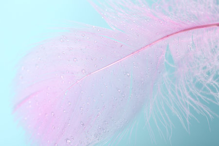 Fluffy pink feather on light blue background, closeup