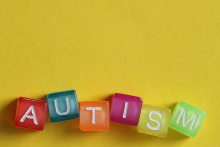 Word Autism made with colorful cubes on yellow background, top view. Space for text