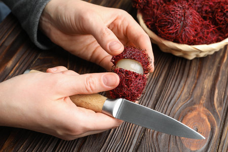 Woman peeling ripe rambutan at wooden table, closeupの写真素材
