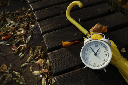 Alarm clock and yellow umbrella on wooden bench outdoors. Space for textの写真素材