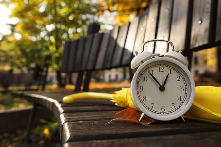 Alarm clock and yellow umbrella on wooden bench outdoors, closeup. Space for textの写真素材