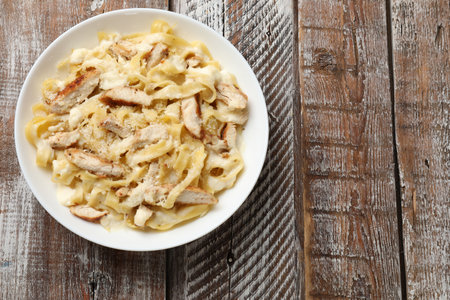 Tasty Alfredo pasta with chicken on wooden table, top view. Space for textの写真素材