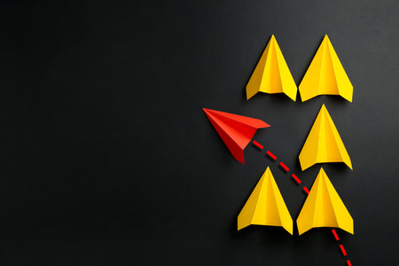 Red paper plane with flight path turning other way, among yellow ones on black background. Dashed line for trajectoryの写真素材