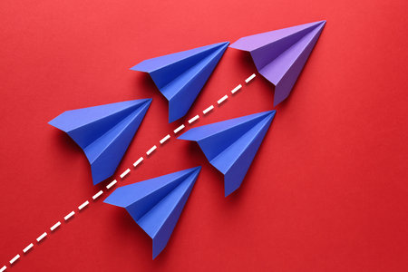 Purple paper plane with flight path among blue ones on red background. Dashed line for trajectory