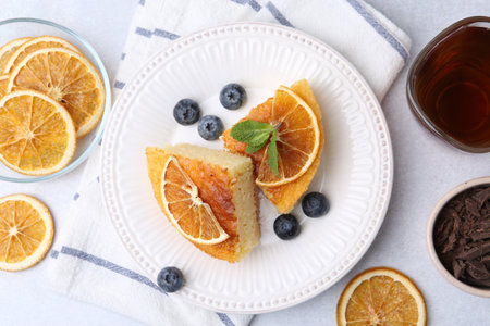 Pieces of delicious semolina cake with blueberries and orange slices on light table, flat layの写真素材