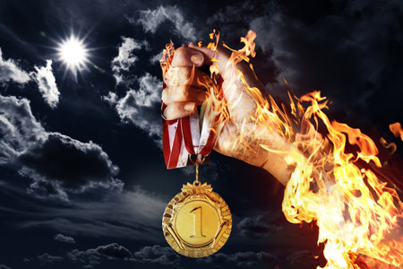 Woman holding gold medal in her flaming hand against darkened sky, closeupの写真素材