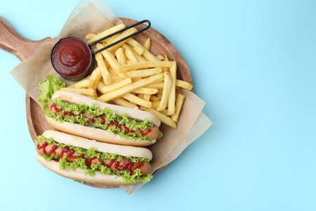 Tasty hot dogs with lettuce, ketchup and potato fries on light blue background, top view. Space for textの写真素材