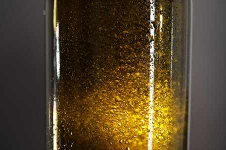 Glass bottle with condensation drops on grey background, closeup