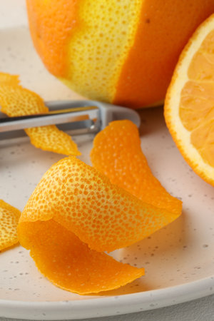 Fresh orange peel, fruit and peeler on light table, closeup