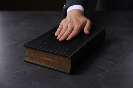 Man taking oath with his hand on Bible at black table, closeupの写真素材