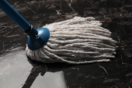 Cleaning black marble floor with string mop, closeup
