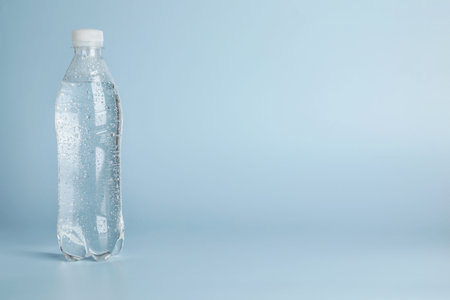 Plastic bottle of water on light blue background, space for text