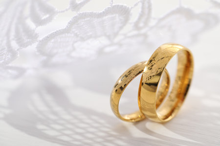 Beautiful golden wedding rings and white lace on light backgroundの写真素材