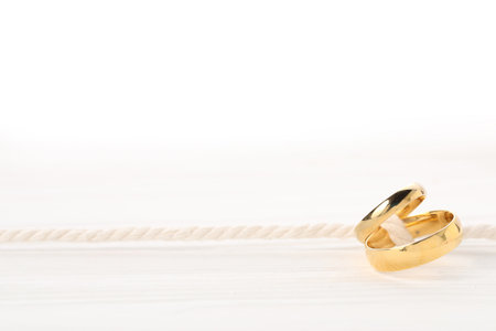 Golden wedding rings tied with string on white wooden background, closeup. Space for textの写真素材