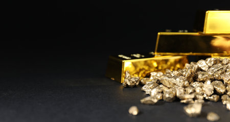 Gold nuggets and bars on black table, closeup. Space for text