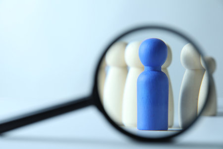 Human resources concept. Looking at wooden figures through magnifying glass on light background, closeup. Space for textの写真素材