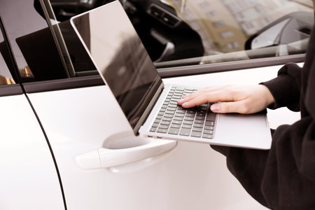 Thief hacking car system with laptop near vehicle, closeupの写真素材