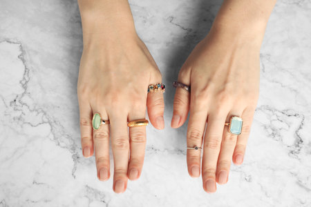 Beautiful bijouterie. Woman wearing different stylish rings at white marble table, top view