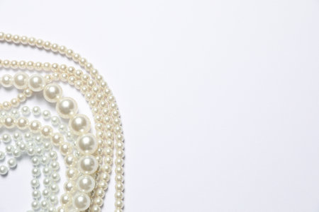 Beautiful pearl necklaces on white background, flat lay. Space for textの写真素材
