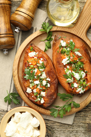 Tasty cooked sweet potatoes with feta cheese, green onion, parsley and oil on wooden board, flat layの写真素材