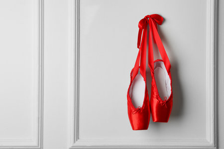 Pair of beautiful red pointe shoes hanging on white wall, space for textの写真素材
