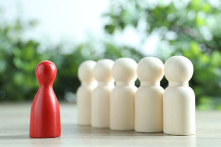 Human resources concept. Red figure in front of wooden ones on table against blurred background, closeupの写真素材