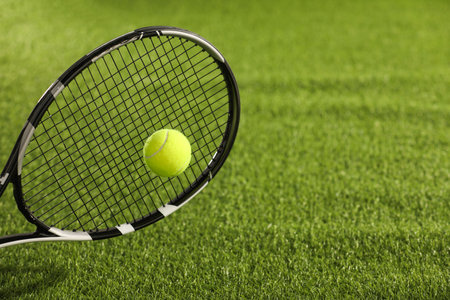 Tennis racket with ball on green artificial grass, closeup. Space for textの写真素材