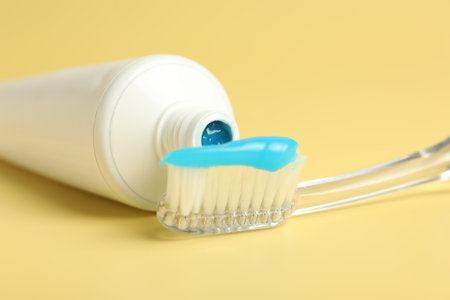 Toothbrush with toothpaste and tube on yellow background, closeup