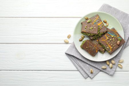 Pieces of Dubai chocolate bars with pistachios and knafeh on white wooden table, flat lay. Space for textの写真素材