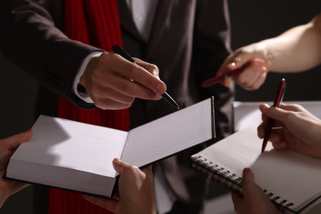 Man signing autograph in book on dark background, closeup
