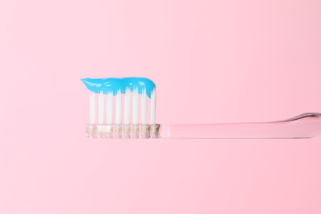 Toothbrush with toothpaste in air on pink background, closeup
