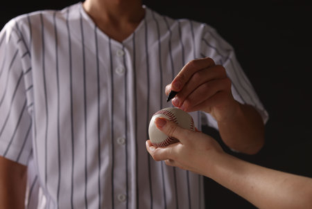 Baseball player signing autograph on ball against black background, closeup