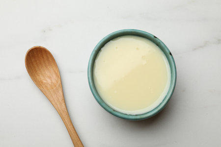 Condensed milk in bowl and spoon on white marble table, top viewの写真素材