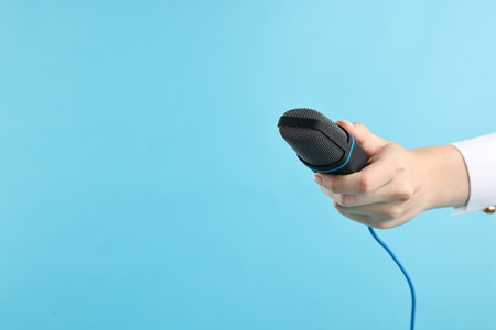 Woman with microphone on light blue background, closeup. Space for textの写真素材