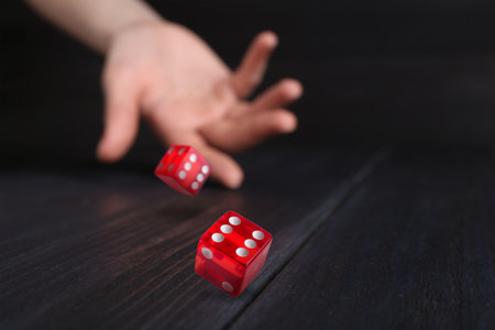 Woman throwing red dice on black wooden table, closeup. Space for textの写真素材