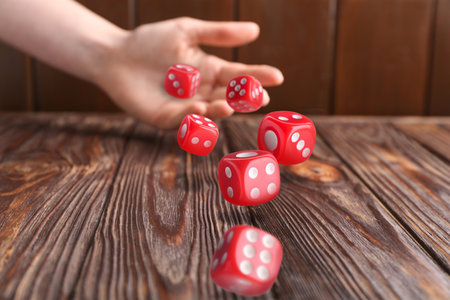 Woman throwing red dice on wooden table, closeupの写真素材
