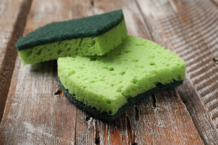 Two green sponges on wooden table, closeup