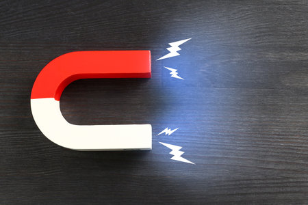 Horseshoe magnet with lightnings on wooden background, top view